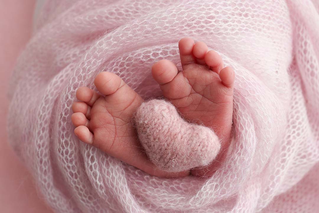 tiny baby feet wrapped in a pink blanket with a wool heart