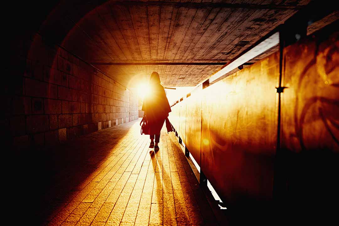 a woman walking towards a golden light the end of a tunnel